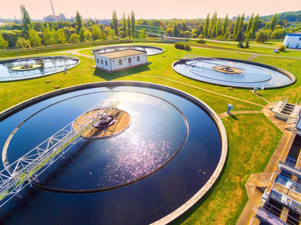 Luftaufnahme einer Wasseraufbereitungsanlage mit mehreren runden Tanks, einem zentralen Gebäude und umgebender Grünanlage.